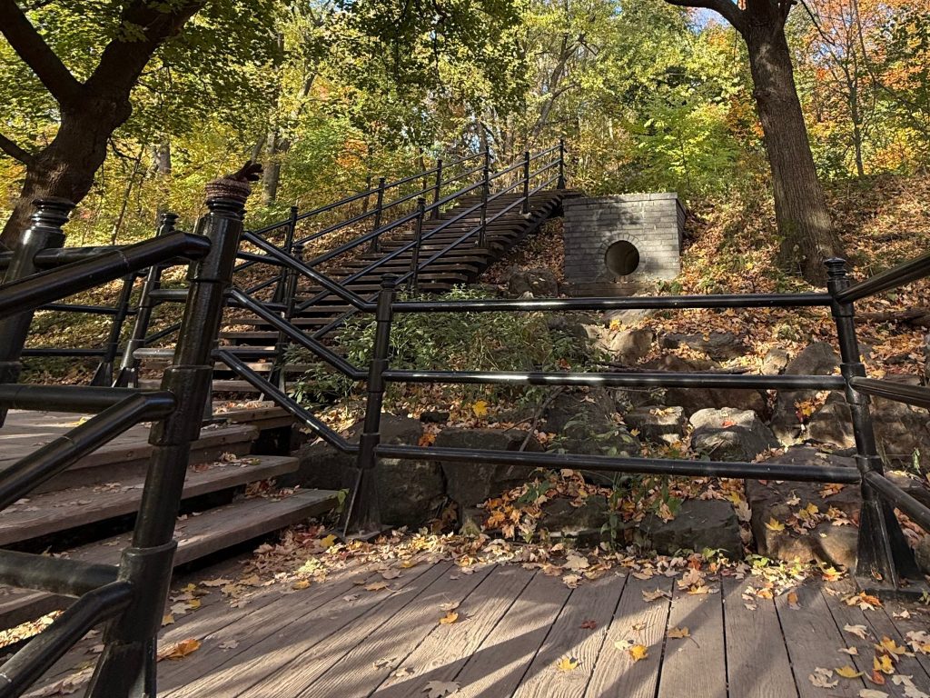 A partially opaque, atmospheric photo of a weathered outdoor wooden staircase ascending through a lush green forest in Montreal. Overlaid in the center is the brand logo and the text: 'I could never' in a bold serif font, followed by the phrase 'until I decided to notice the wonder in every step' in an elegant, modern italic font.